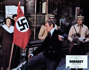 Brian (Michael York) openly kicks Nazi propaganda rally (Cabaret, 1972)